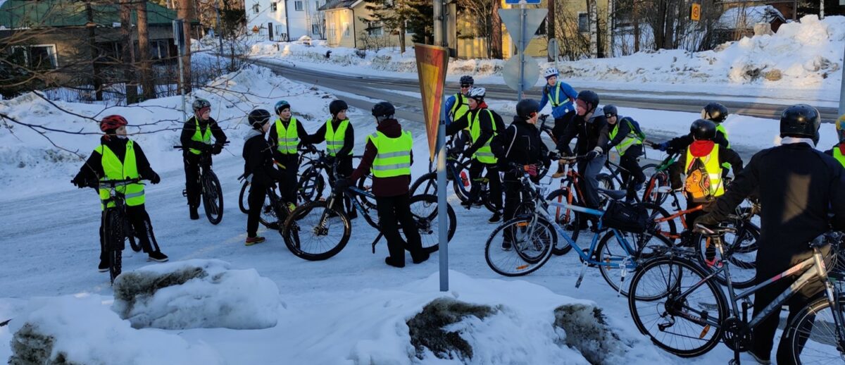 Joukko ihmisiä seisoo pyörien kanssa tien risteyksessä talvella.