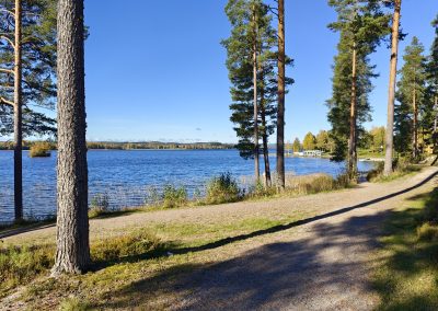 Taustalla järvi ja puita, edessä hiekkatie.